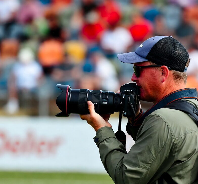 عکاس ورزشی در کنار زمین فوتبال در حال تمرکز بر جریان بازی برای پیش‌بینی لحظه حساس گل.