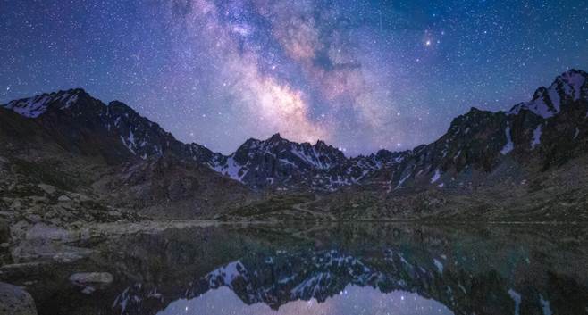 راهنمای جامع عکاسی از آسمان شب: از انتخاب مکان تا تنظیمات حرفهای 1 تصویری خیرهکننده از کهکشان راه شیری بر فراز یک منظره کوهستانی در شب