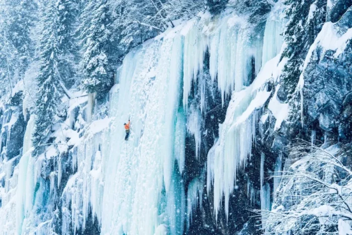 تصویر یک کوهنورد را نشان می‌دهد که بر روی دیواره یخ در حال صعود است.
