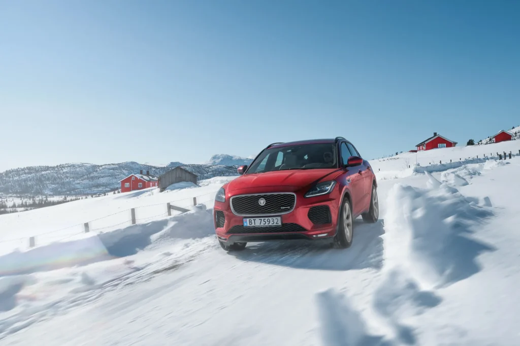 ماشین قرمز سریعاً در حال حرکت در جاده برفی است.