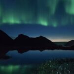 نمایشی خیره‌کننده از شفق قطبی رنگین که بر فراز قله‌های کوهستان برفی رقص می‌کند