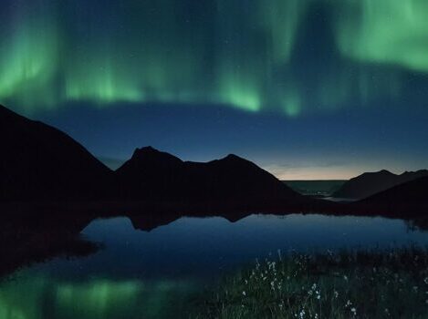 نمایشی خیره‌کننده از شفق قطبی رنگین که بر فراز قله‌های کوهستان برفی رقص می‌کند