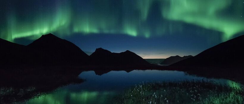 نمایشی خیره‌کننده از شفق قطبی رنگین که بر فراز قله‌های کوهستان برفی رقص می‌کند