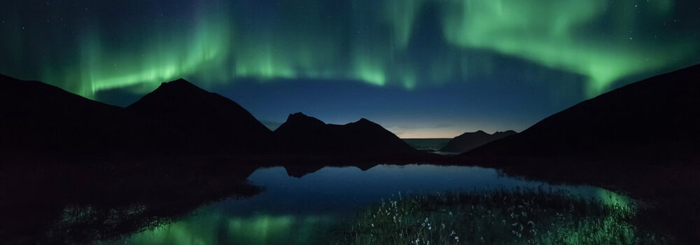 نمایشی خیره‌کننده از شفق قطبی رنگین که بر فراز قله‌های کوهستان برفی رقص می‌کند