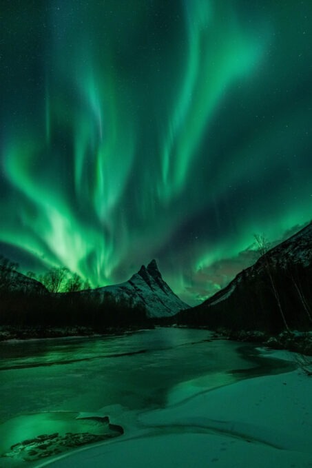 بازتاب زیبای نورهای سبز شفق قطبی در سطح آرام یک دریاچه یا رودخانه. 